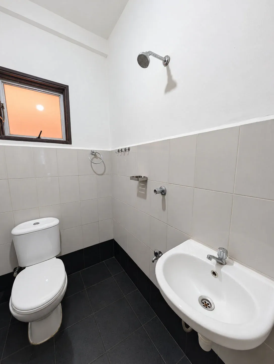En-suite bathroom with shower, toilet, wall-mounted basin and handheld bidet sprayer on grey floor tiles