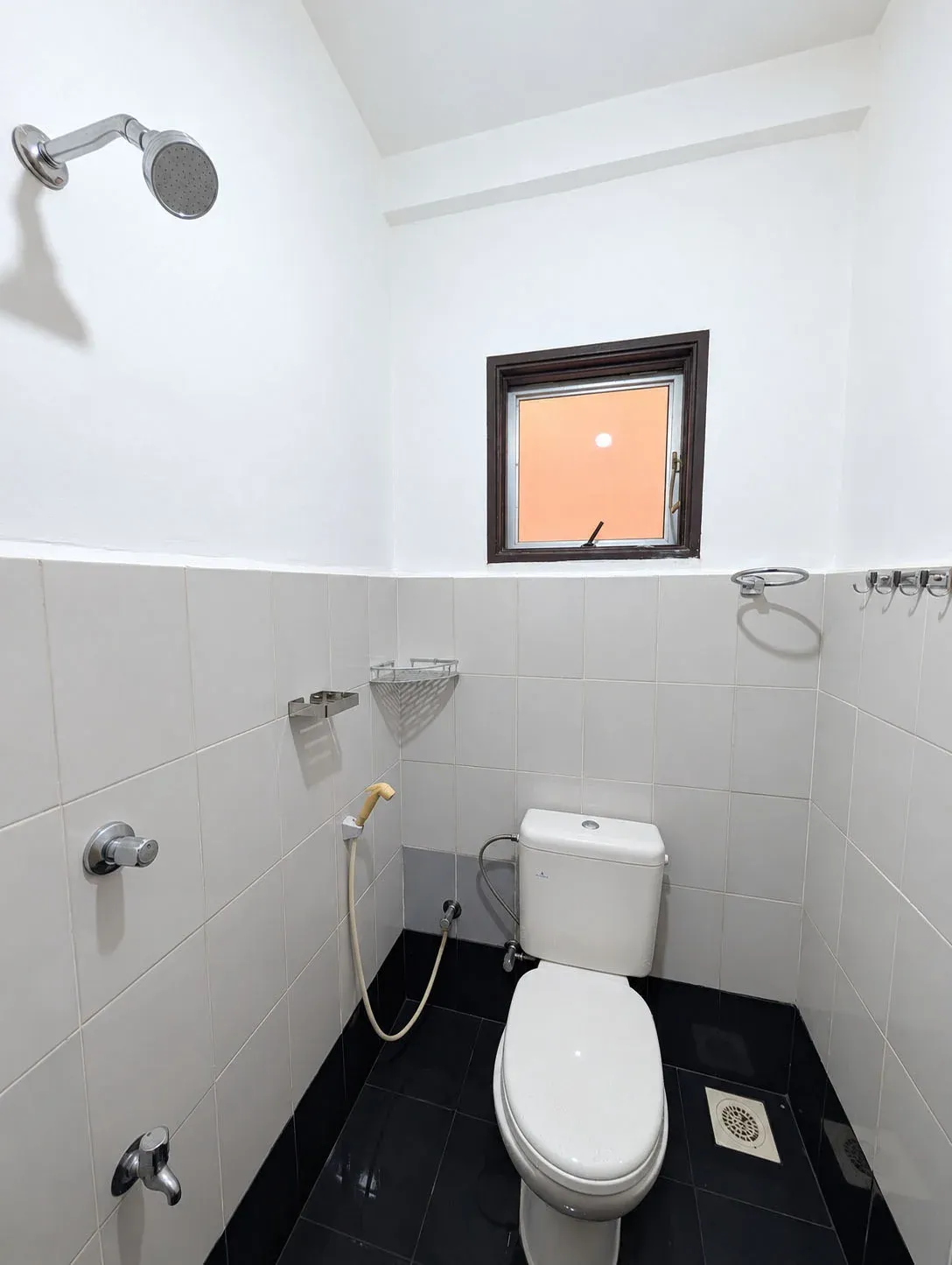 Shared bathroom with shower, dual-flush toilet and handheld bidet sprayer, white wall tiles and black floor tiles