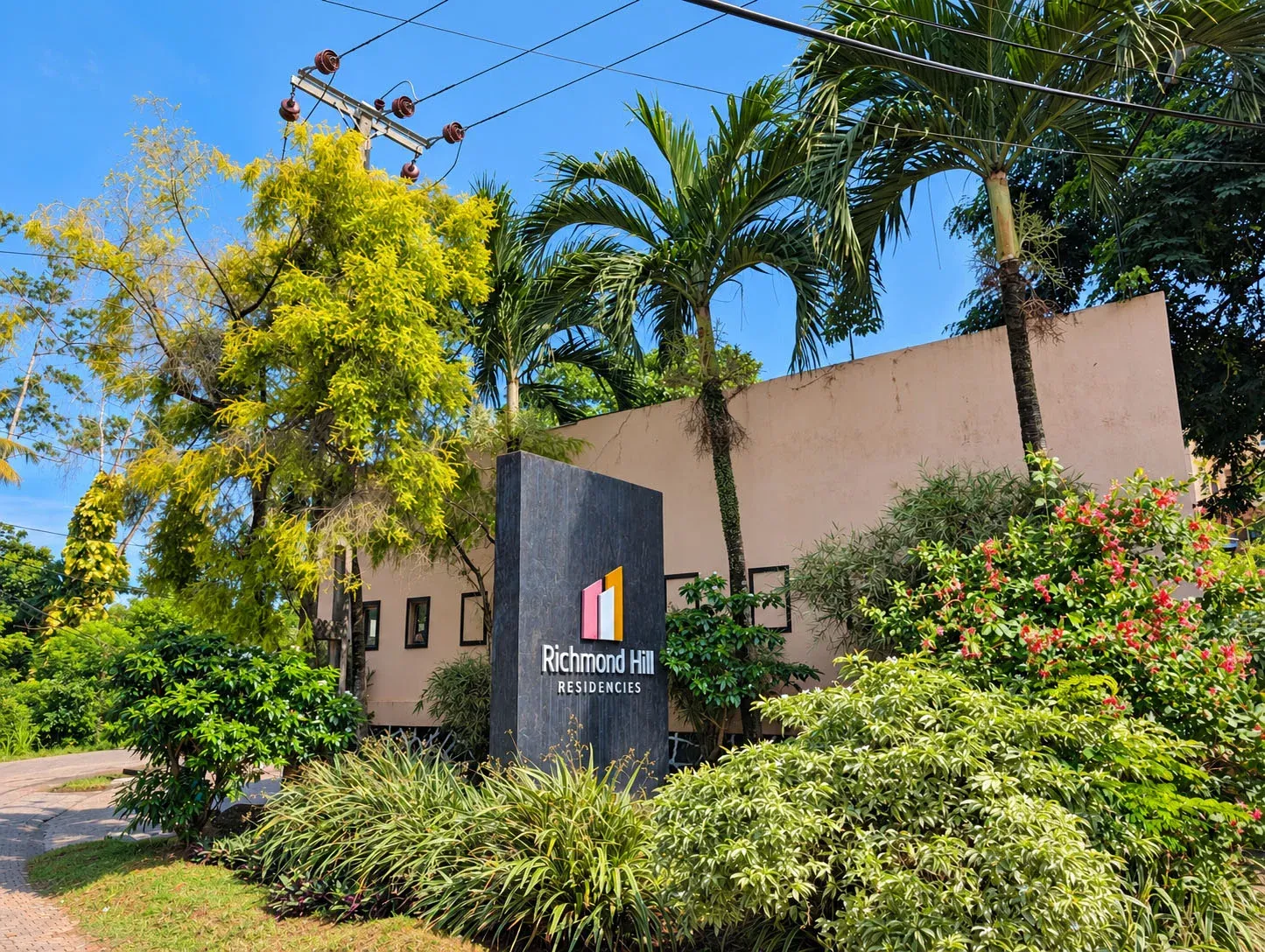 Richmond Hill Residencies entrance sign among palms and flowering shrubs under a blue sky